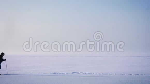 宽镜头的男性背包客的轮廓在雪地上向右行走视频的预览图