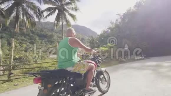 成年男子骑着摩托车在绿色山丘上的乡村道路上行驶覆盖着热带森林旅行的人骑着视频的预览图