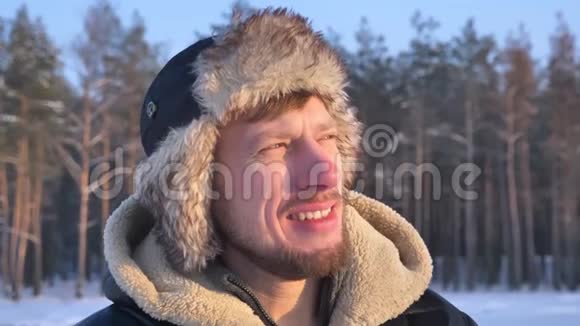 在冬天的森林背景下穿着兜帽和外套的探险家在镜头中欢乐地微笑着近距离观看视频的预览图