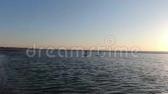 两个女人站在冲浪板上划水背景是日落4K视频的预览图