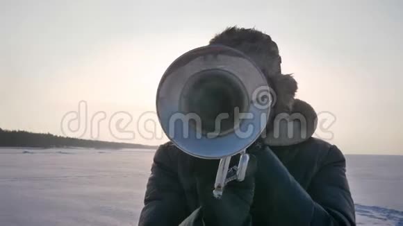 严肃的白种人音乐家在冰冻的自然背景下在阳光下吹喇叭的特写肖像视频的预览图