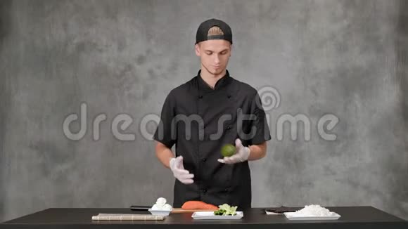 年轻的厨师穿着黑色衣服在灰色背景下做饭厨房餐桌日本寿司和卷的原料视频的预览图