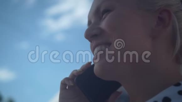 穿着白衬衫和黑豆的白人商务女性在电话里对着蓝天和云彩说话视频的预览图