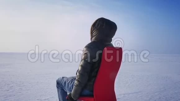 婴儿商人穿着温暖的外套头罩在冰冻的湖面上坐在红色的椅子上旋转视频的预览图
