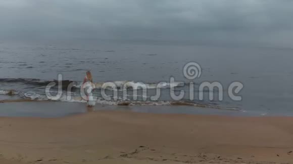 空中侧景美丽的金发女郎在海边漫步一位穿着白色连衣裙的海滩仙女与视频的预览图
