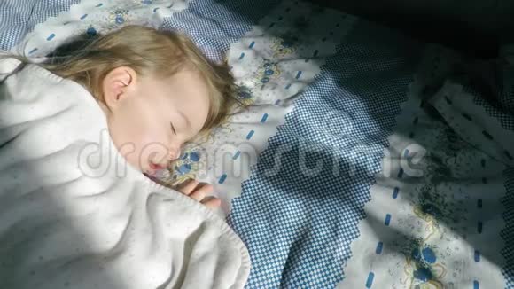 一个金发的小女孩正睡在床上被阳光照亮视频的预览图