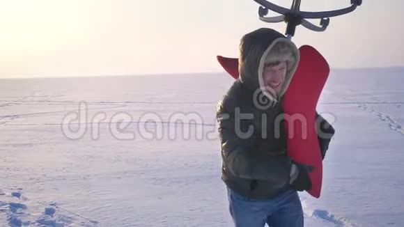 近镜头运动员穿着温暖的外套和引擎盖骑着一把沉重的红色椅子在他的肩膀上雪地背景视频的预览图