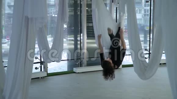 美丽的女人在瑜伽吊床上徘徊在工作室里摆出不同的姿势周围有许多白色的空吊床现代视频的预览图