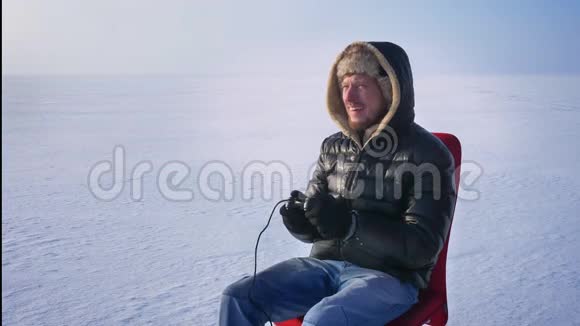 一幅商人穿着温暖的外套和引擎盖在冰冻湖背景上玩游戏的肖像视频的预览图