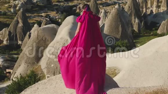 穿着紫色长裙的女孩站在卡帕多西亚的岩石上视频的预览图
