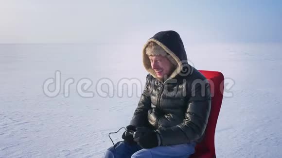 穿着保暖外套和引擎盖的男性玩家在视频游戏中获胜并在冰冻湖背景下极度高兴地举起双手视频的预览图