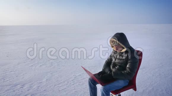 穿着保暖外套和头罩的商人坐在雪地里手提电脑双手放在头上看着太阳视频的预览图