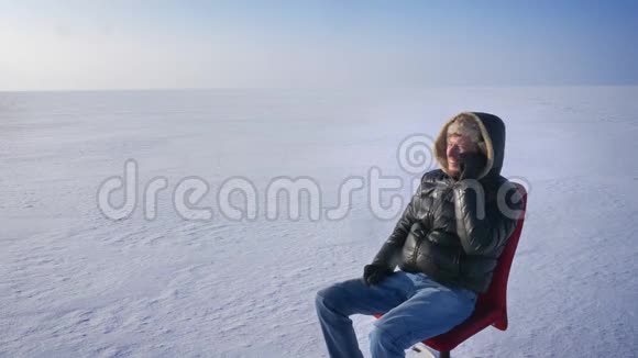 穿着温暖外套和引擎盖的商人坐在雪地里用手机愉快地交谈微笑着视频的预览图