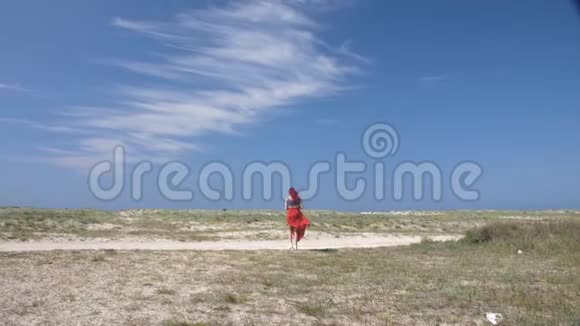 一个穿着红色裙子的女孩走在沙滩上背景是无尽的蓝天视频的预览图