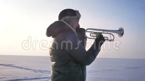 绕着中年白种人音乐家的镜头在冬天的自然背景下积极地吹喇叭视频的预览图