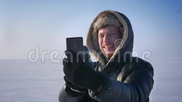 在雪漠的智能手机上穿着温暖外套和引擎盖的商人在视频游戏中愉快地交谈的特写肖像视频的预览图