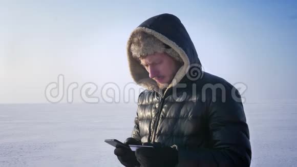 商人穿着温暖的外套和引擎盖站在冰冻的湖面上用信用卡和智能手机进行交易视频的预览图