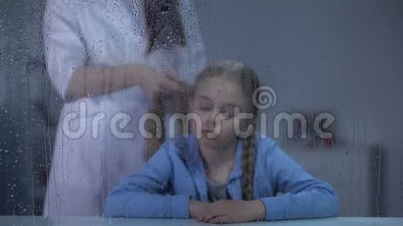保姆编织小女孩的头发在雨窗后在孤儿院照顾美丽视频的预览图