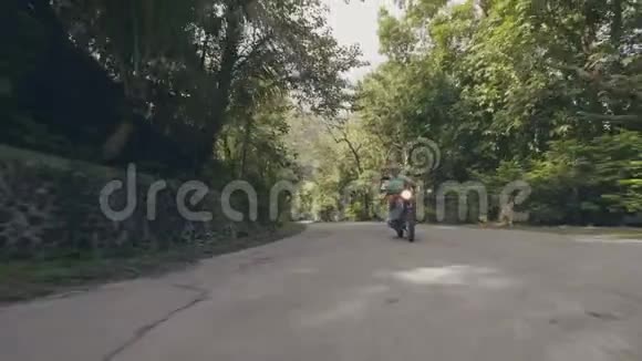 成年男子骑摩托车骑摩托车在郊区道路上的绿树景观骑摩托车旅行的老人视频的预览图