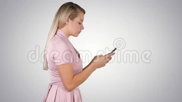 穿粉色连衣裙的漂亮女人在渐变背景下用智能手机发短信视频的预览图
