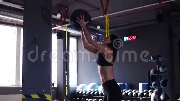 一个年轻的健康女性在一个深色的现代运动中把一个药球扔到墙上锻炼的侧视镜头视频的预览图