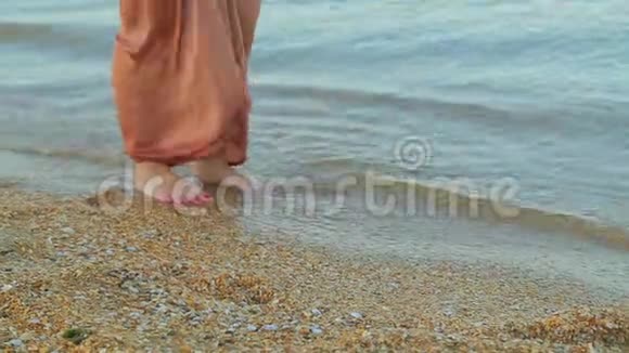 穿着宽大裤子的女腿赤脚沿着海水的边缘走视频的预览图