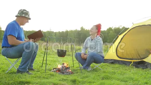 一个男人和一个女人在靠近火炉的帐篷附近的空地上做晚饭视频的预览图