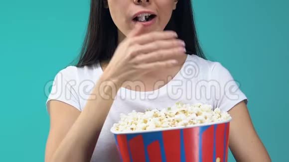 带着爆米花的年轻女人专心看电视节目暴饮暴食垃圾食品视频的预览图