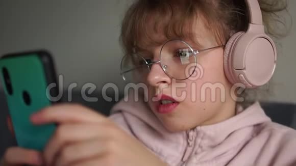 亲密画像卷曲可爱少女青春亚文化戴眼镜的女学生带着电话听音乐视频的预览图