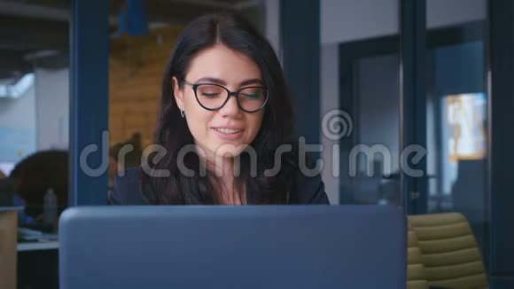 女商人高兴地微笑着看着办公室里的摄像机年轻女性在办公桌上使用笔记本电脑视频的预览图