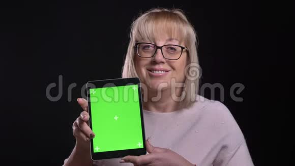 用平板电脑拍摄戴眼镜的老白种人金发女性的特写镜头用绿色屏幕拍摄微笑视频的预览图