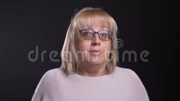 一位戴眼镜的老白种人金发女性在直视背景摄像机时感到困惑视频的预览图