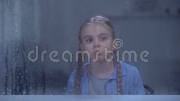 伤心的小女孩透过雨窗看着镜头被父母遗忘了视频的预览图