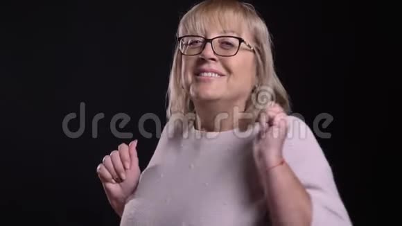 特写镜头拍摄戴眼镜的老白种人金发女性在镜头前与背景一起跳舞和玩视频的预览图
