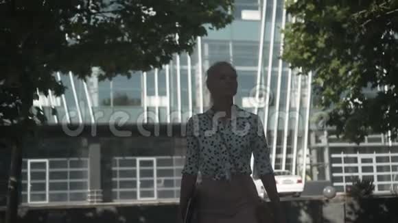 商务女性穿着一件白色衬衫上面有黑豌豆手里拿着一台笔记本电脑走在办公楼附近的街道上视频的预览图