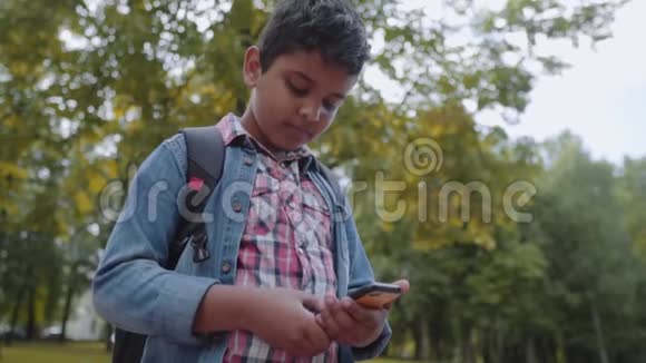 户外肖像美国快乐学校男孩与智能手机年轻的学生看着手机回到学校视频的预览图