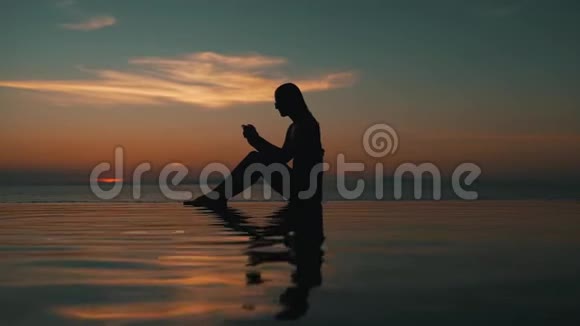 女孩在海边日落时使用智能手机视频的预览图