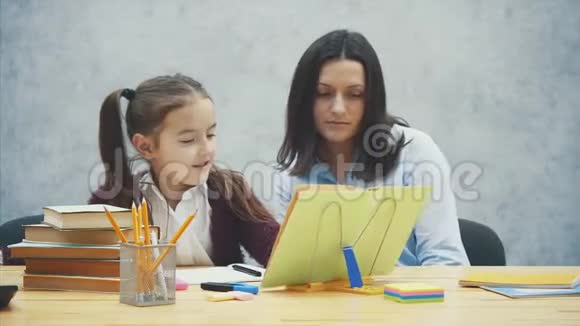 妈妈和女儿坐在桌子旁看书在这灰色背景下视频的预览图
