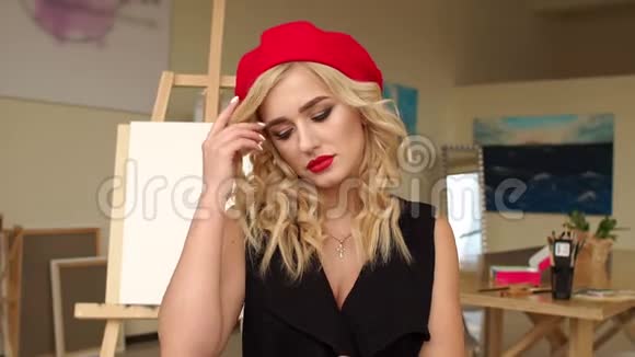 一位年轻的金发女艺术家红唇在工作室里画椅子视频的预览图