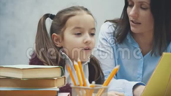 妈妈和女儿坐在桌子旁看书在这灰色背景下视频的预览图