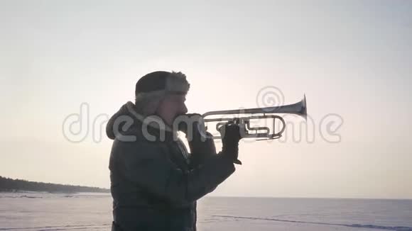 在冰冻的自然背景下独自一个高加索音乐家在阳光下积极吹喇叭的肖像视频的预览图