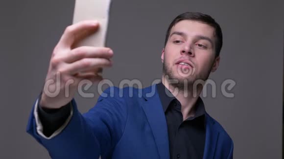 年轻英俊的白种人在手机上自拍的特写镜头背景是灰色的视频的预览图