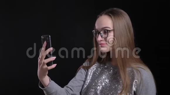 眼镜中年轻迷人的时髦女性的特写镜头在手机上打视频电话背景被隔离视频的预览图