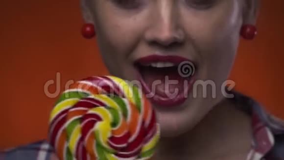 性感的金发碧眼的红唇女郎正在摆姿势舔她五颜六色的棒棒糖视频的预览图