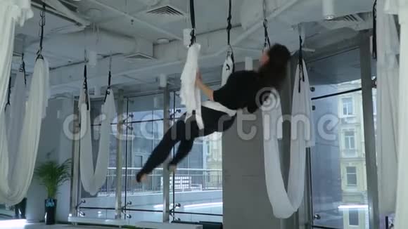 身材魁梧的漂亮女人头朝下吊在现代健身中心的瑜伽吊床上地板很大视频的预览图