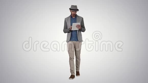 英俊的微笑阿拉伯男子戴着帽子走路和使用平板电脑的梯度背景视频的预览图