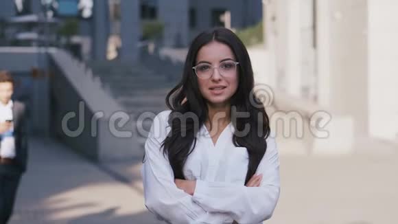 年轻漂亮的商业女性戴着眼镜站在现代办公楼附近看着相机微笑着视频的预览图