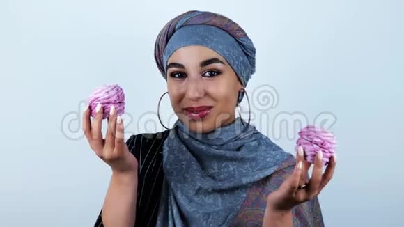 年轻美丽的阿拉伯女人微笑着双手拿着美味的纸杯蛋糕在孤立的白色背景上视频的预览图