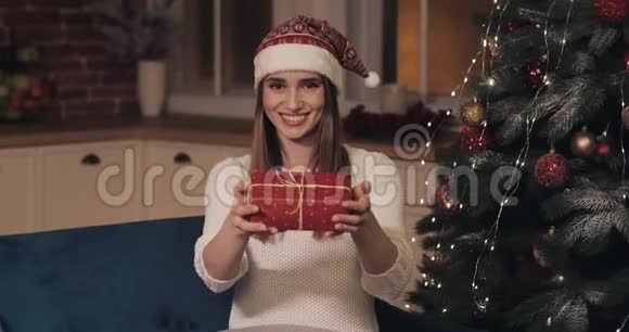 戴着圣诞帽坐在沙发上的年轻白种人妇女在科西家圣诞树旁的画像视频的预览图