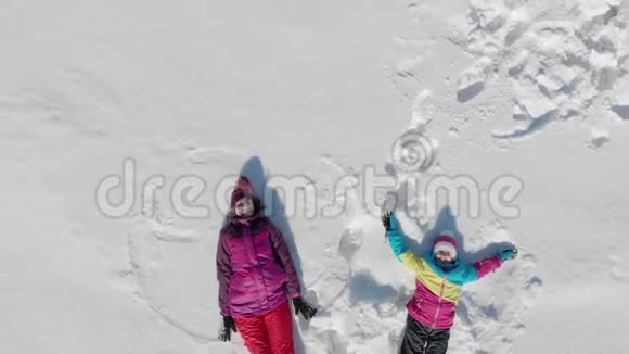 年轻的母亲和小女儿在雪地上做天使阳光明媚的冬日欢乐的家庭尽情欢乐视频的预览图
